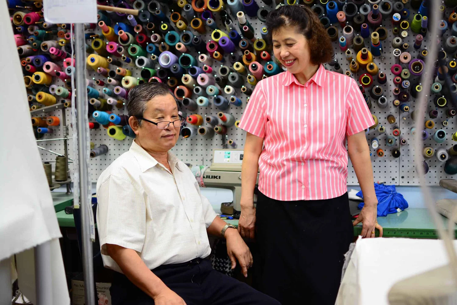 Two people in Sun’s Tailor workroom with sewing equipment and colorful thread